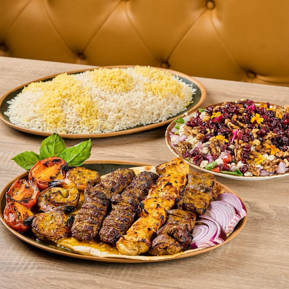 Persian kabob platter with grilled meats, vegetables, rice, and a colorful salad on a wooden table.