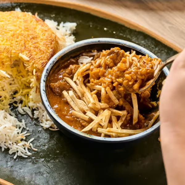 A close-up of Gheymeh stew with crispy fries, rice, and golden Tahdig on a dark plate.
