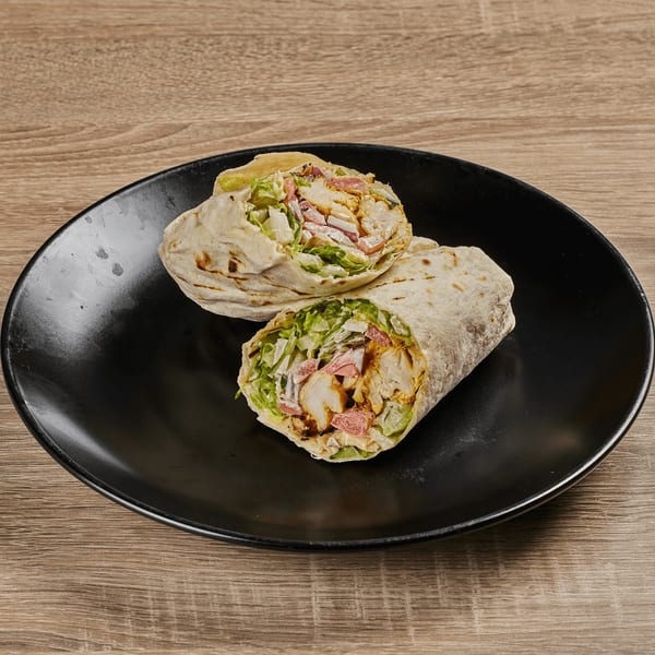 Two Persian chicken wraps, filled with meat, lettuce, and sauce, on a black plate.