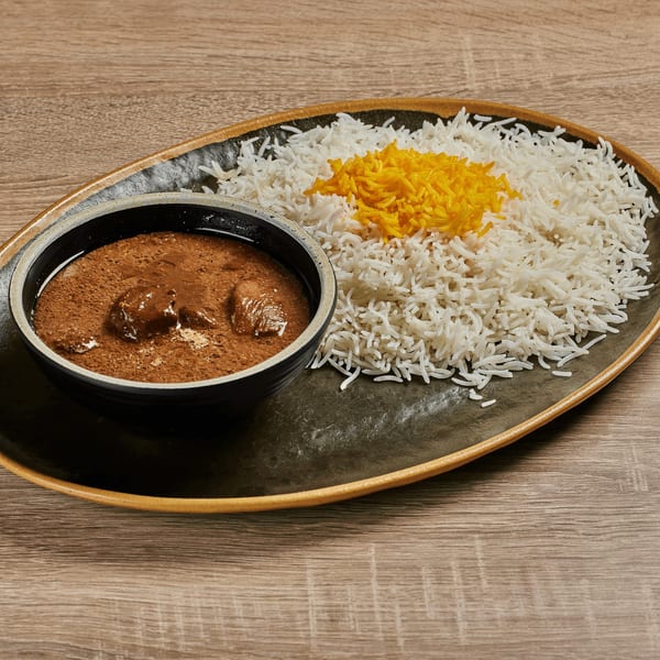 Persian Fesenjan stew with chicken and white rice topped with saffron, served on a dark plate.