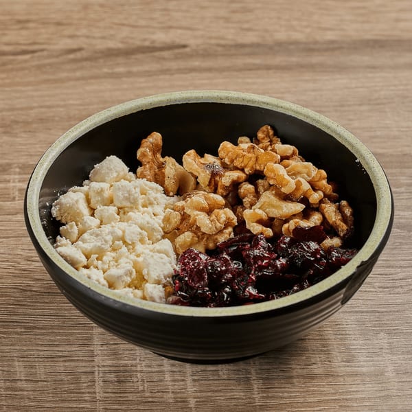 A black bowl filled with feta cheese, walnuts, and dried cranberries on a wooden table.