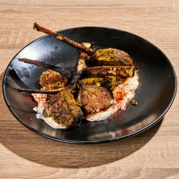 Grilled lamb chops with spices and a creamy sauce, served on a black plate.