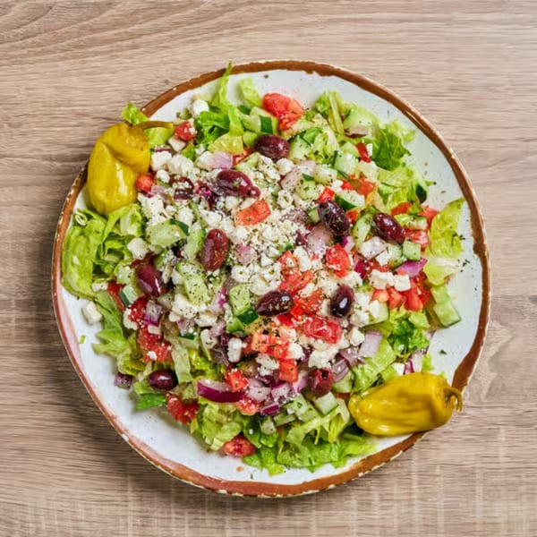 A vibrant Persian salad with lettuce, tomatoes, cucumbers, red onions, feta, olives, and two yellow peppers.