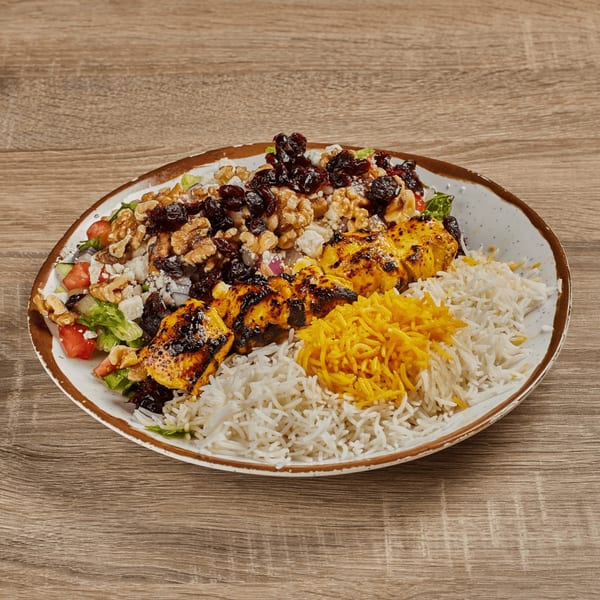 Persian chicken kabob with white and saffron rice, salad, walnuts, and raisins on a plate.