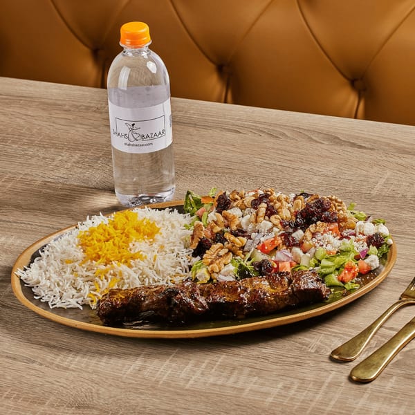 Persian kabob with saffron rice, a fresh salad topped with walnuts and feta, and bottled water.