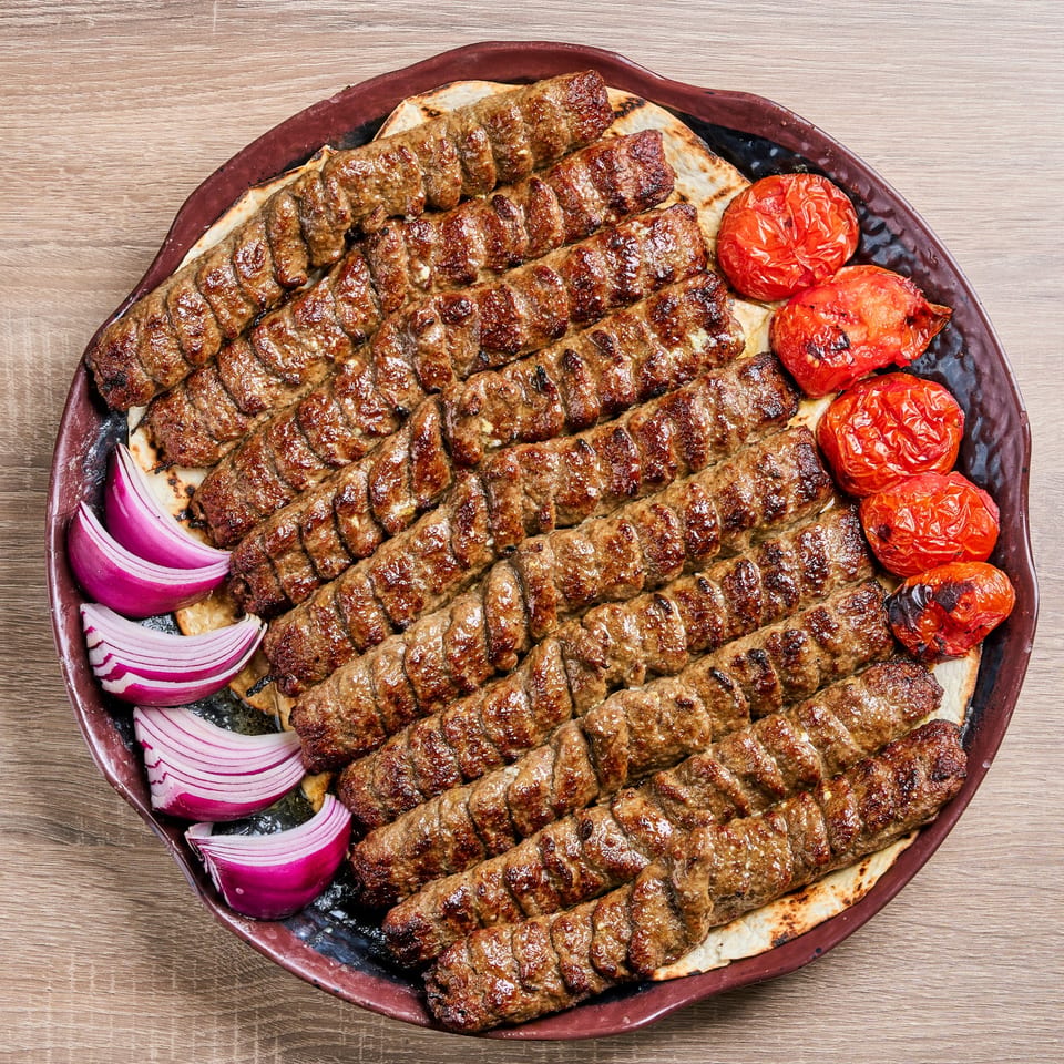 Shahs of Kabob's Persian koobideh kabobs with roasted tomatoes and red onion on a platter.