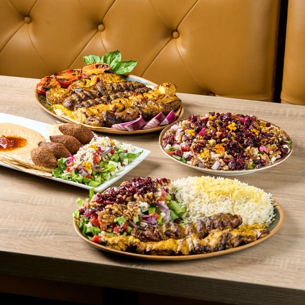 A table laden with various Persian dishes, including kebabs, rice, salads, and hummus.