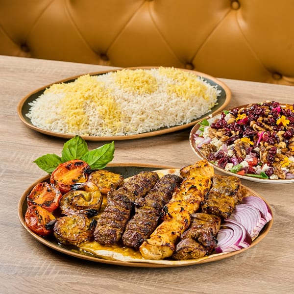 Persian kabob platter with grilled meats, vegetables, rice, and a colorful salad on a wooden table.