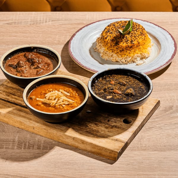 Three bowls of Persian stews and a plate of saffron rice with tahdig on a wooden table.